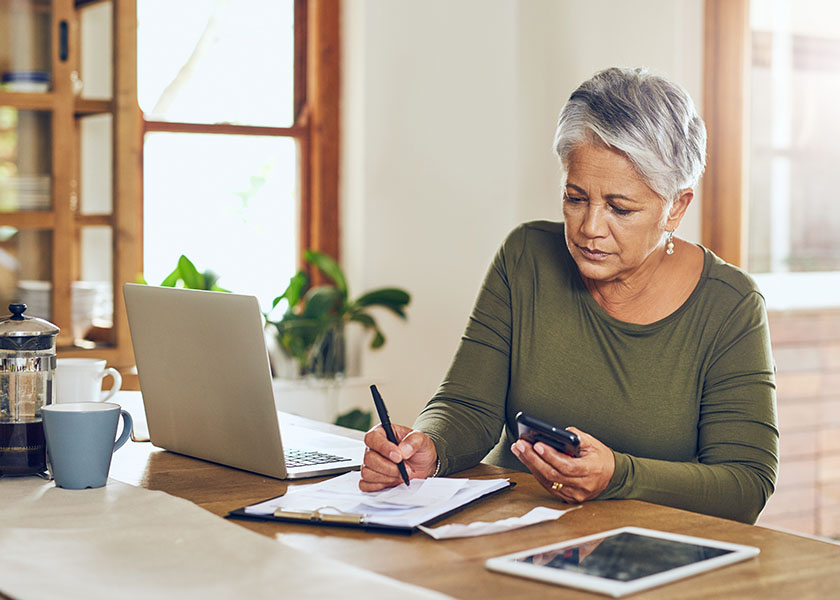 Woman sitting at kitchen table working on taxes with a laptop and smartphone