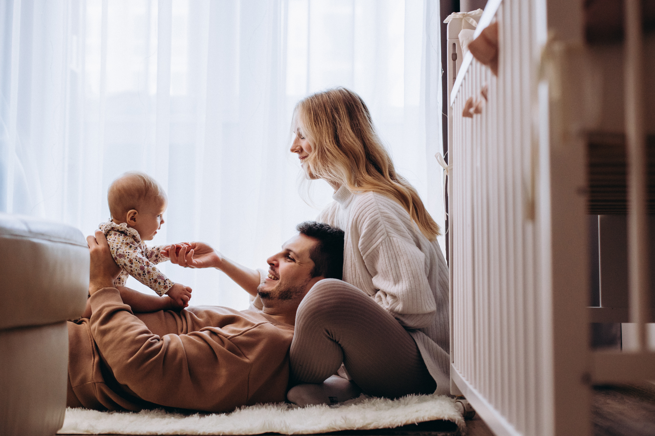 Parents on the floor next to a crib, playing with their infant.